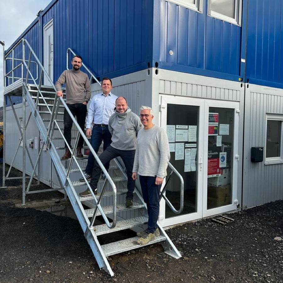 Der vier Verantwortlichen der Zukunft Mittelahr AöR stehen auf einer Stahltreppe vor blauen und grauen Bürocontainern.